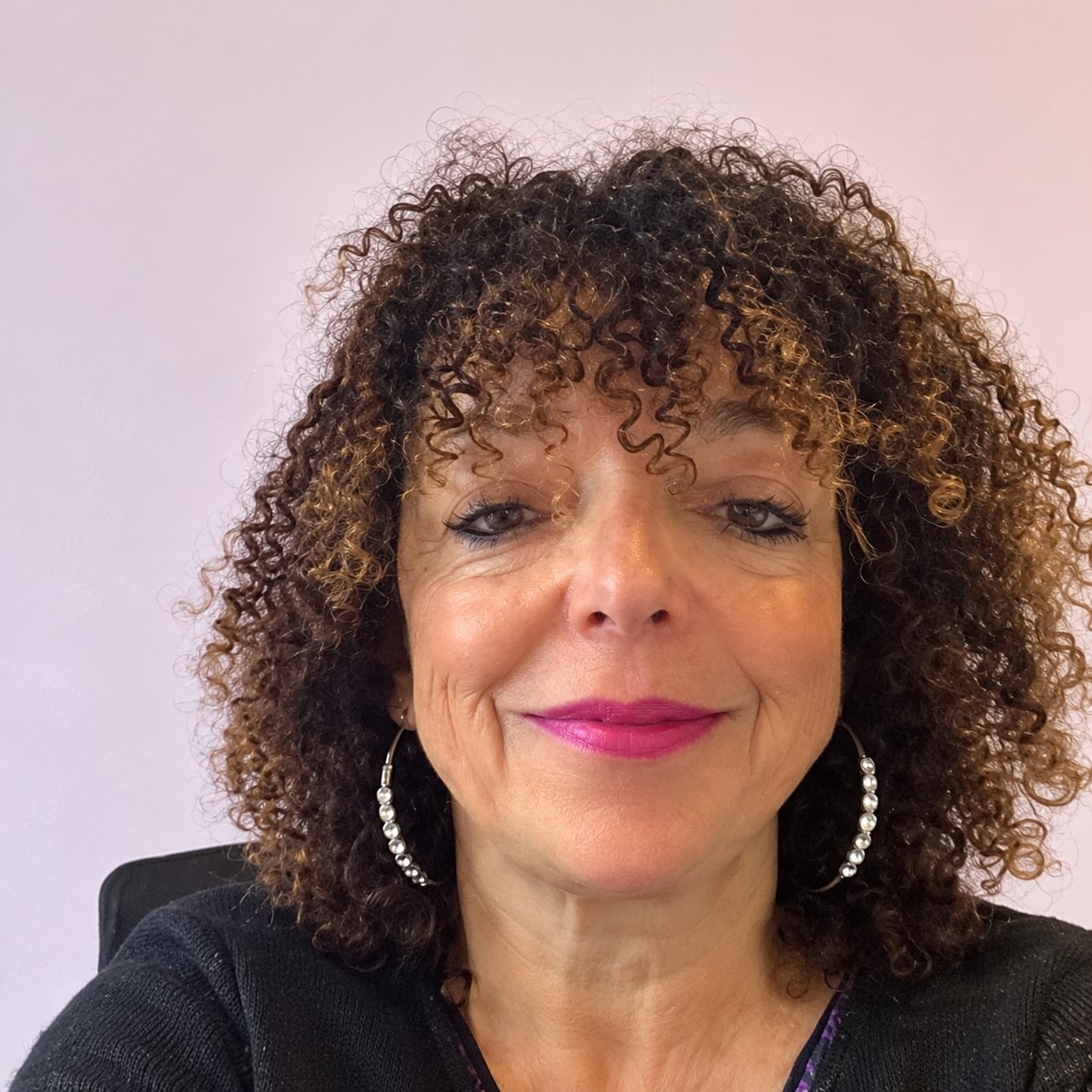 Portrait d’une femme aux cheveux bouclés devant un mur rose pâle